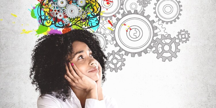 Smiling young African American woman in white shirt looking at colorful brain sketch with gears drawn on concrete wall. Concept of brainstorming