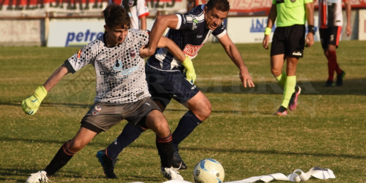 PUJA. El arquero de Ex Alumnos 185 intenta cortar el avance de Pablo Motta, que no le quita la mirada a la pelota.