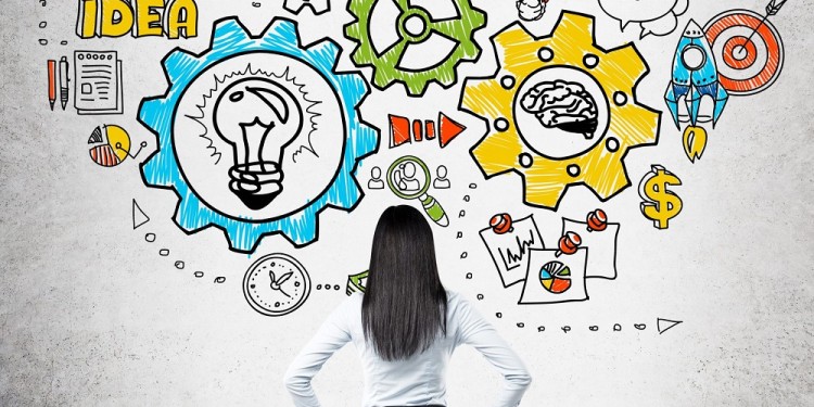 Businesswoman in suit is standing in front of concrete wall with back to camera and looking at sketch with abstract images thinking about business. Concept of right strategy.