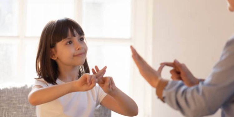 Mom communicating with deaf daughter focus on kid sitting on couch in living room make fingers shape hands talking nonverbal. Hearing loss deaf disability person sign language learning school concept