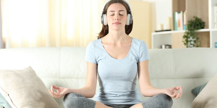 Front view of a woman with headphones listening tutorial meditating doing yoga on a couch at home