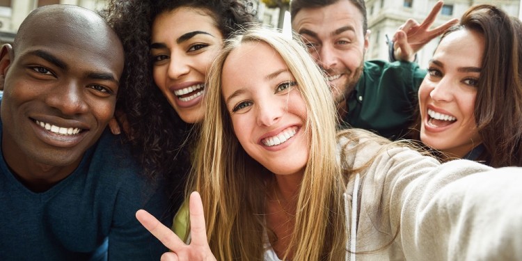 Multiracial group of friends taking selfie in a urban street with a blonde woman in foreground. Three young women and two men wearing casual clothes.