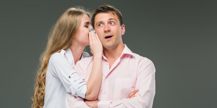 Portrait of a young couple standing against gray studio background. woman whispering in man ear