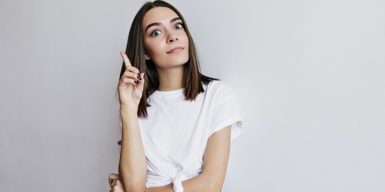 Joyful lady with dark eyes funny posing in studio. Female model in white t-shirt making faces during photoshoot.
