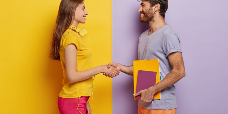Happy groupmates meet after holidays, shake hands, agree to work together as team, stand in profile, lovely woman with headphones meets friend. Unshaven young man holds notepad talks with female