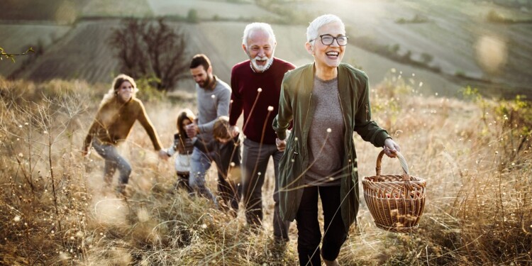 Happy mature woman holding hands with her family while moving up the hill towards their picnic place.