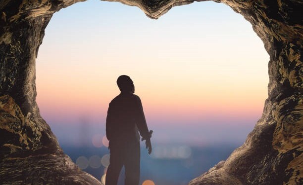 International human rights day concept: Silhouette alone man standing on cave of heart against blurred city sunrise background