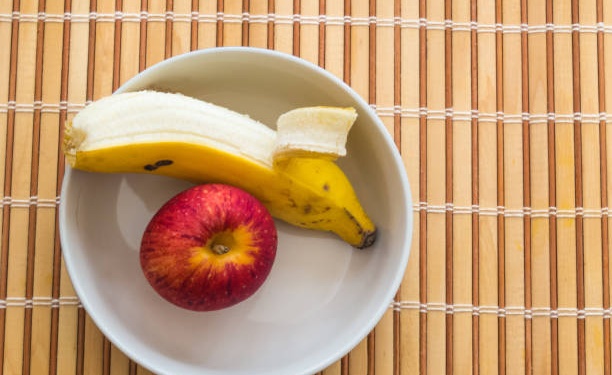 Healthy snack of banana and apple inside white bowl on wooden table