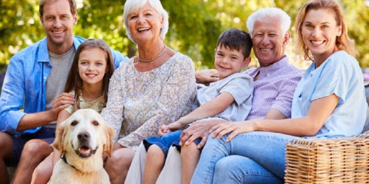 Three generation family sitting with pet dog in the garden