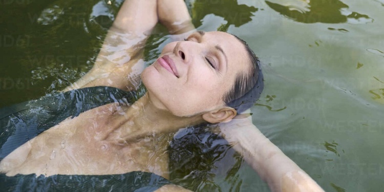 Woman with hands behind head floating on water in lake